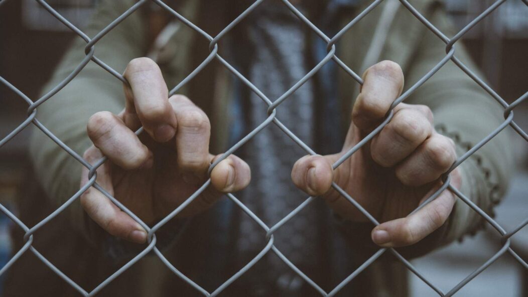 Detained immigrant holding fence symbolizing F-1 visa fraud victims facing inadmissibility and legal battles