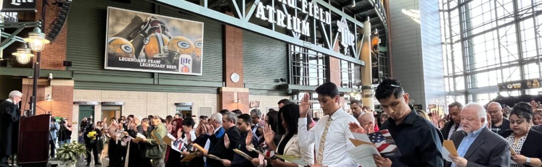 Immigrants taking the Oath of Allegiance during a naturalization ceremony in a large atrium, symbolizing the path to U.S. citizenship.