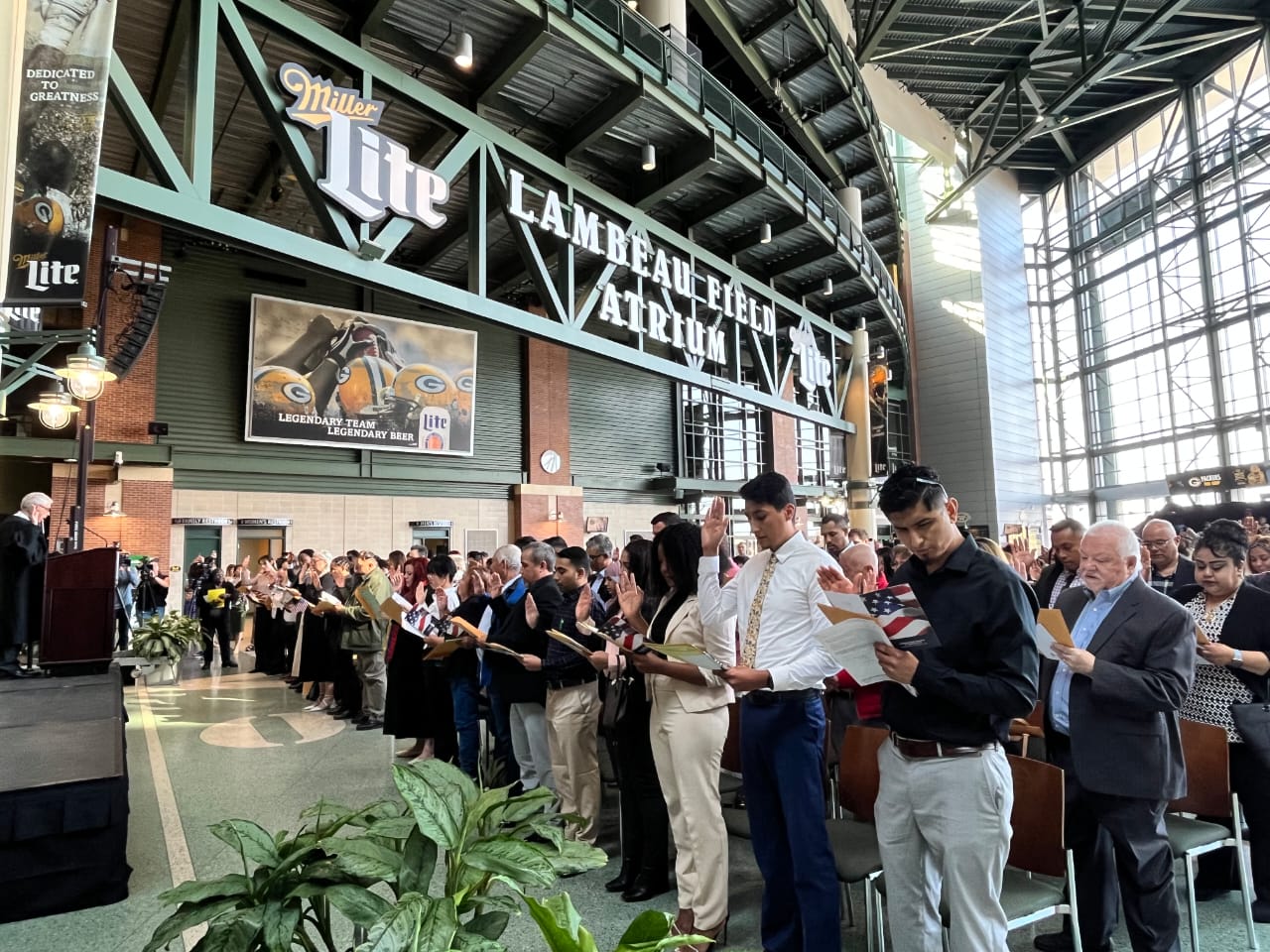 Immigrants taking the Oath of Allegiance during a naturalization ceremony in a large atrium, symbolizing the path to U.S. citizenship.