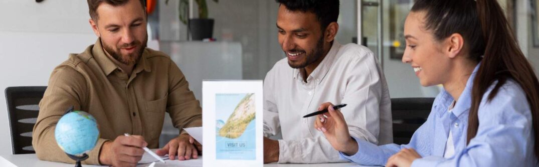 A diverse team of three people sitting around a table, working on travel documents in a modern office environment, with a globe and a travel agency flyer on the table.