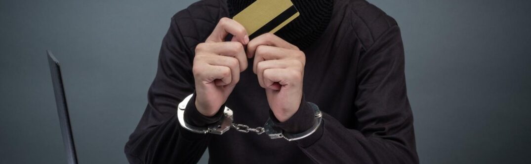 H-1B visa fraud concept with a man in handcuffs holding a credit card in front of a laptop, symbolizing illegal practices and consequences.