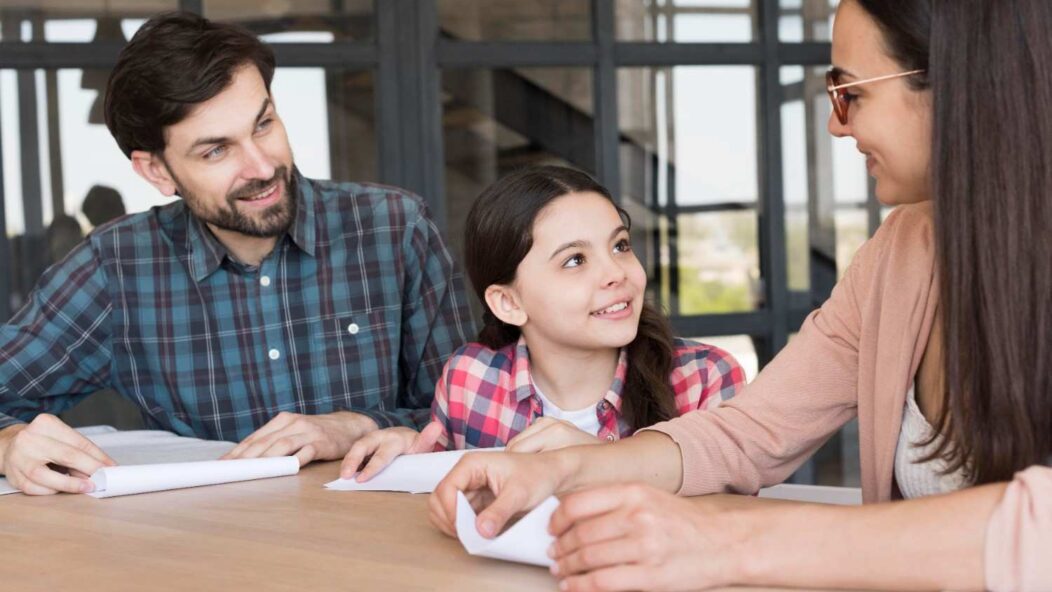 A family discussing citizenship documents with their child in a bright, modern office. The parents and child are smiling and engaged.