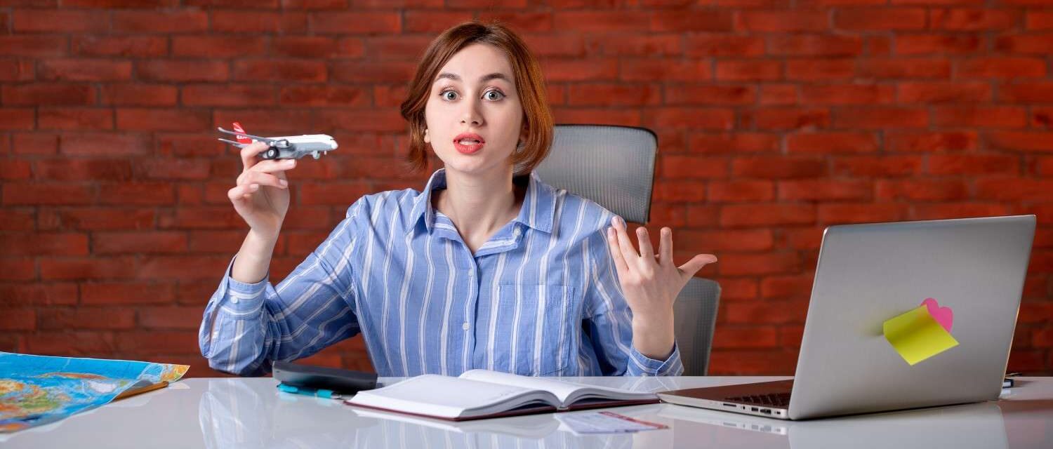 Concerned woman holding a toy airplane, seated at a desk with maps, laptop, and notebooks, representing visa application challenges.