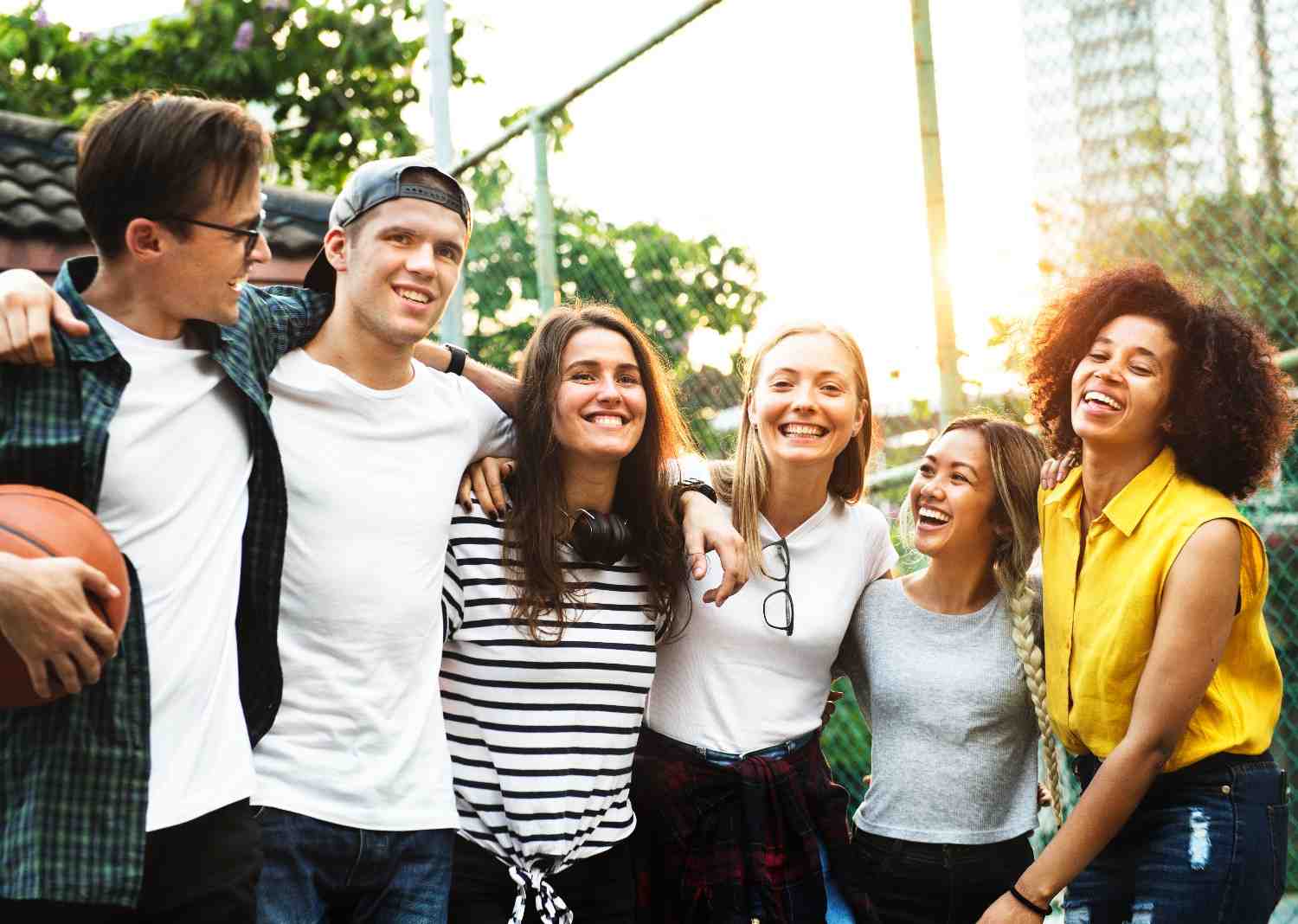 A diverse group of young adults smiling and bonding outdoors, symbolizing inclusivity, connection, and shared experiences.