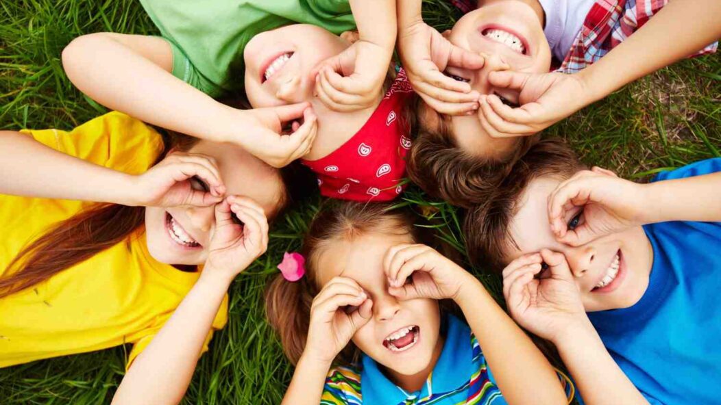 A group of cheerful children lying on the grass, smiling and playing together, symbolizing childhood joy and innocence amidst challenges.