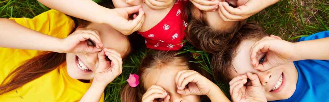 A group of cheerful children lying on the grass, smiling and playing together, symbolizing childhood joy and innocence amidst challenges.