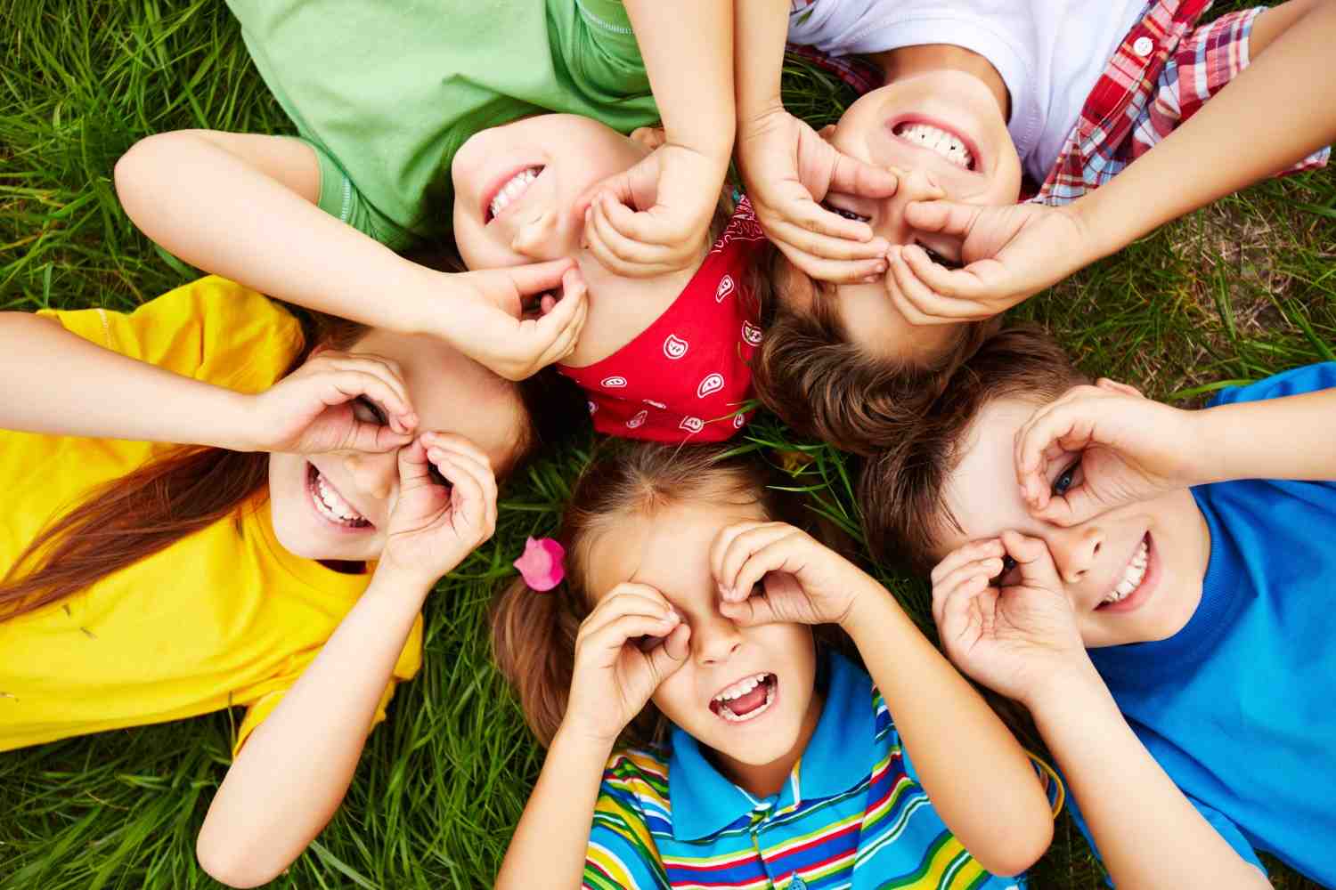 A group of cheerful children lying on the grass, smiling and playing together, symbolizing childhood joy and innocence amidst challenges.