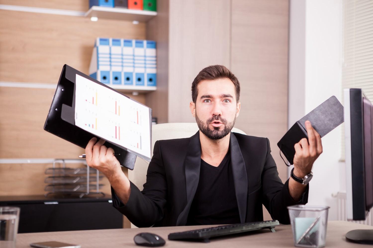 A professional man in an office holding a clipboard with charts and a notebook, expressing frustration, symbolizing challenges in navigating complex processes such as EB-1 visa applications.
