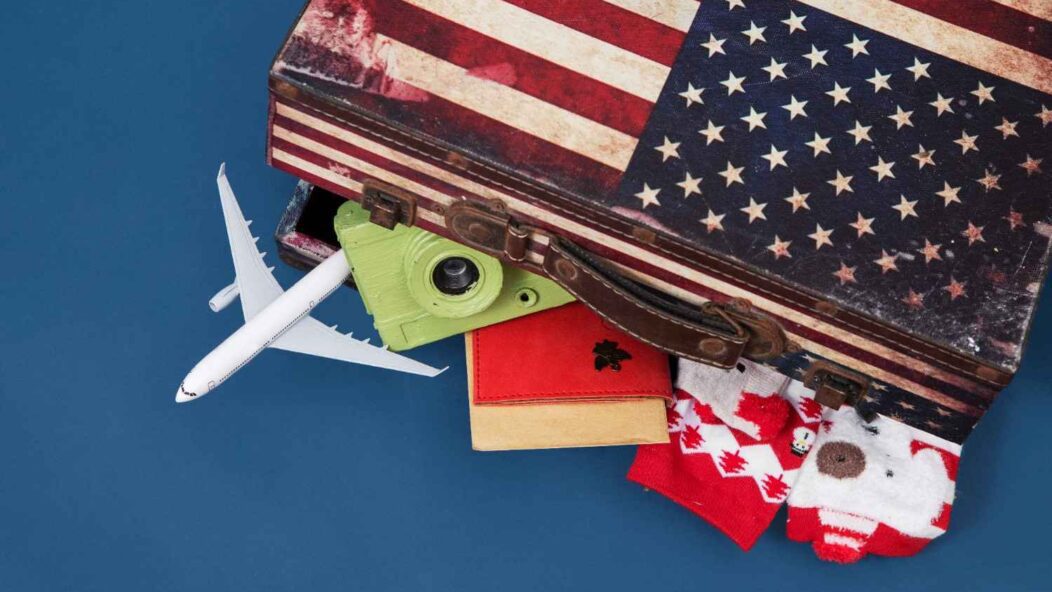 A suitcase featuring the American flag, with items like a toy airplane, a green camera, a red passport, and holiday socks sticking out, symbolizing travel, immigration, and holiday spirit.