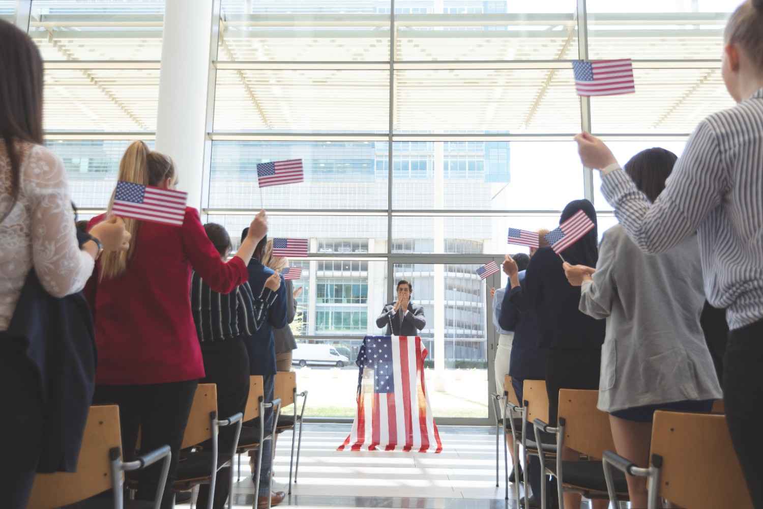 New citizens at a naturalization ceremony in the United States, raising their hands to take the Oath of Allegiance with U.S. flags in the foreground.