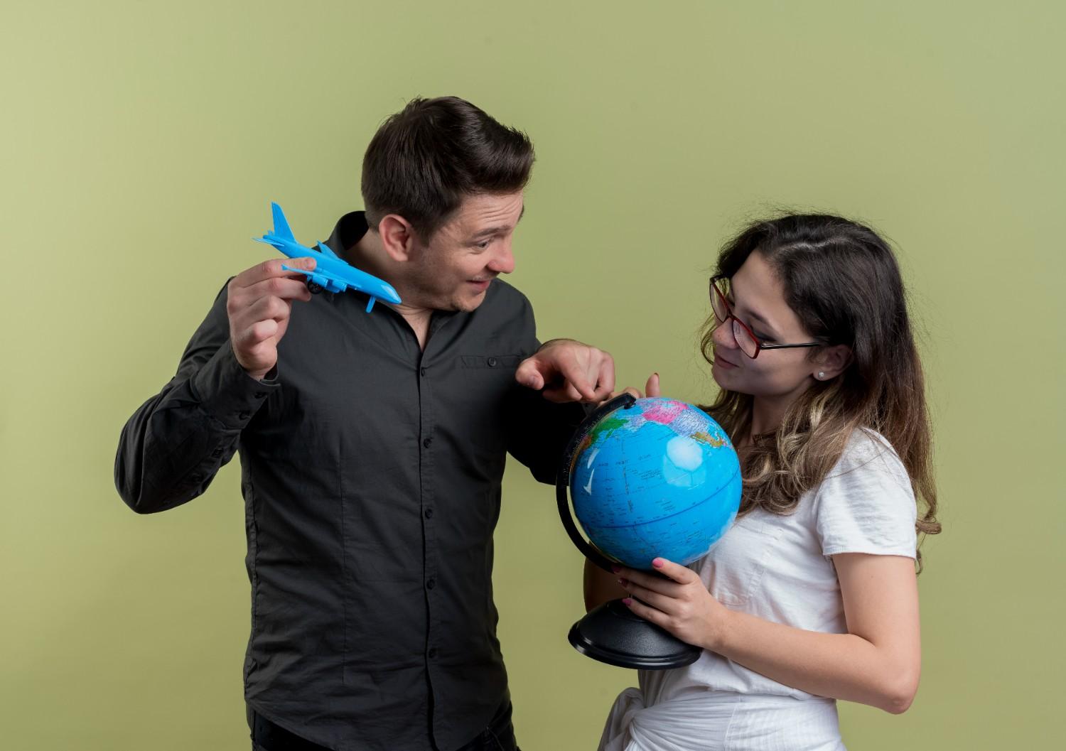 Man holding a toy airplane pointing at a globe with a woman, symbolizing global opportunities for J-1 visa holders.