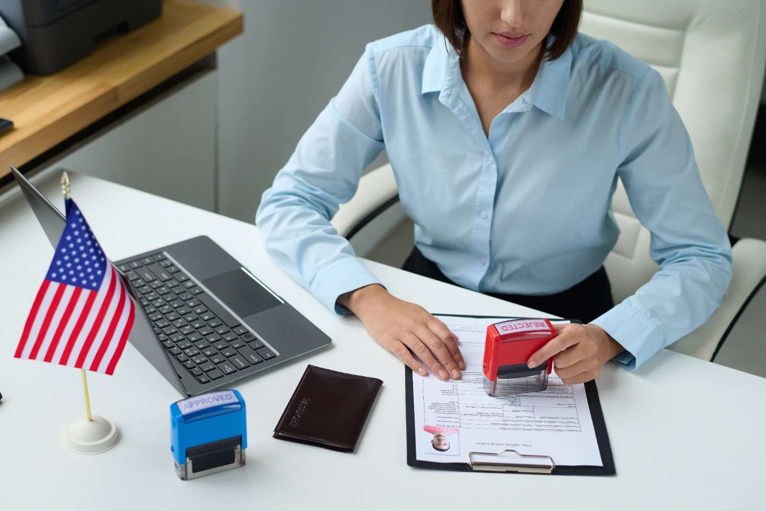 Young woman surprised with a phone in hand, standing in front of the U.S. flag, symbolizing visa-related queries and challenges.