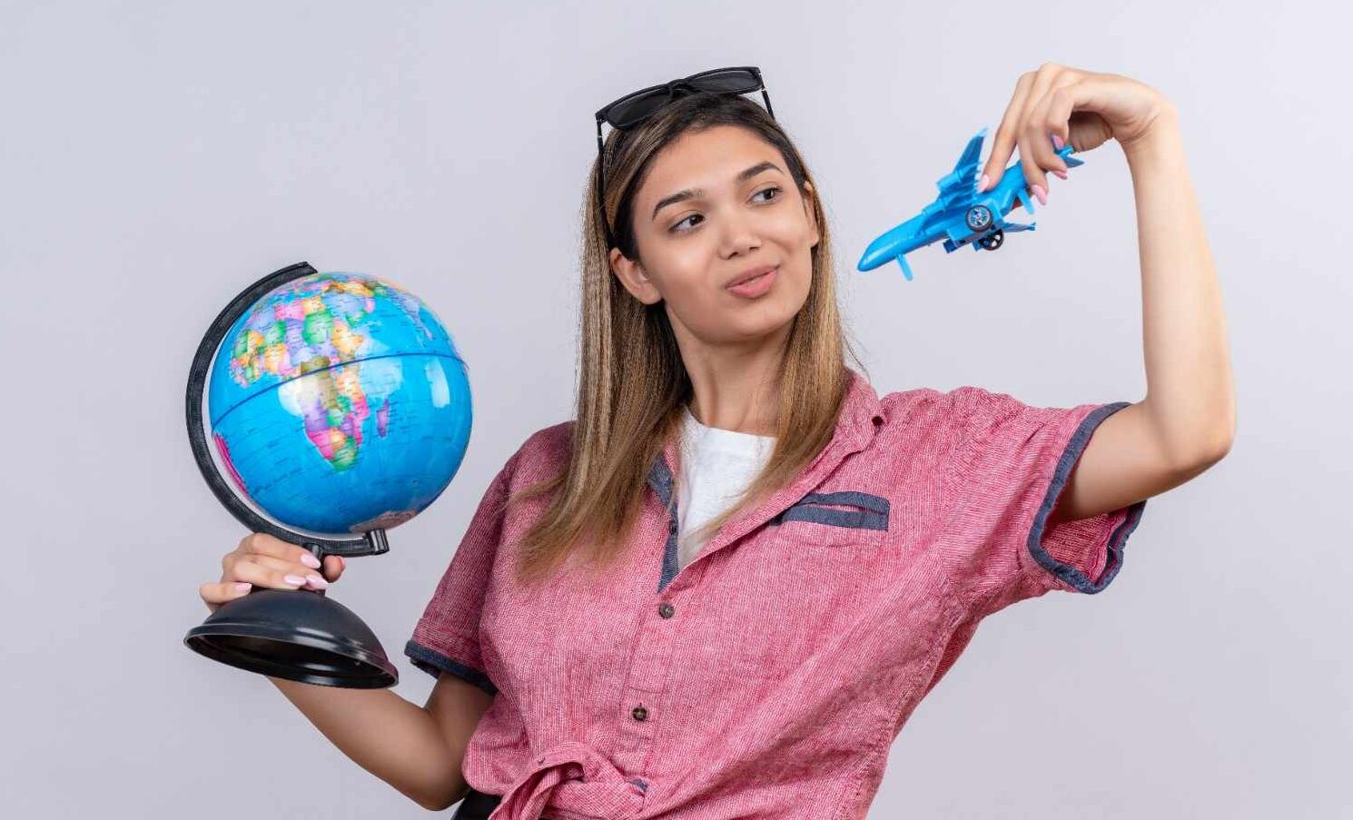 A young woman holding a globe in one hand and a toy airplane in the other, symbolizing travel and opportunities across the world.