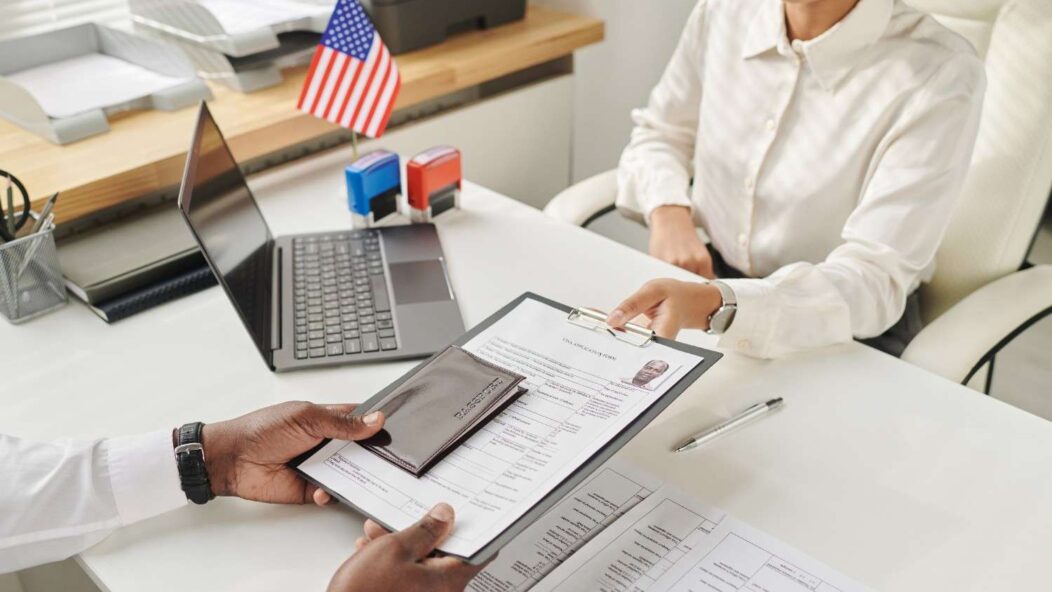 A surprised traveler holding visa documents next to a pink suitcase, symbolizing a Section 221g visa refusal and uncertainty.