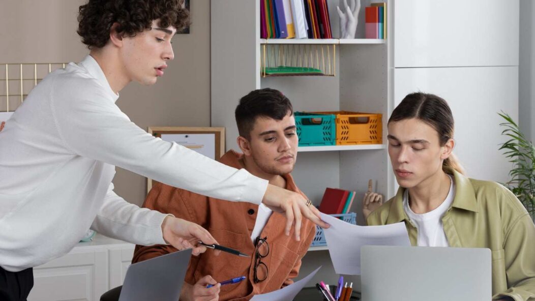 International students discussing self-employment opportunities on OPT with laptops and documents in a modern workspace.