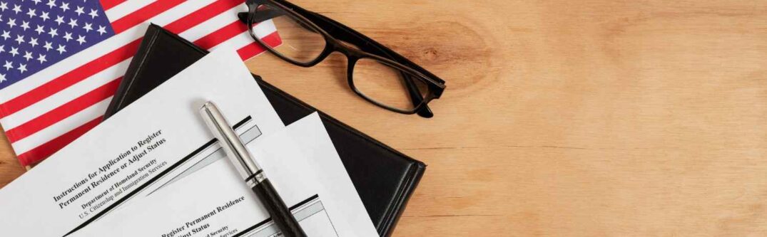 USCIS application forms with American flag and glasses on a wooden desk.