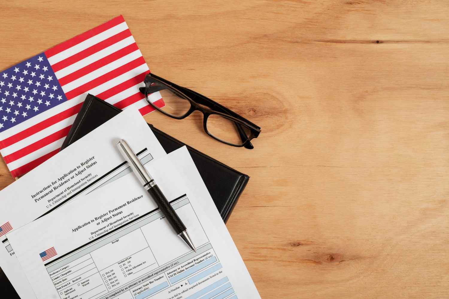 USCIS application forms with American flag and glasses on a wooden desk.
