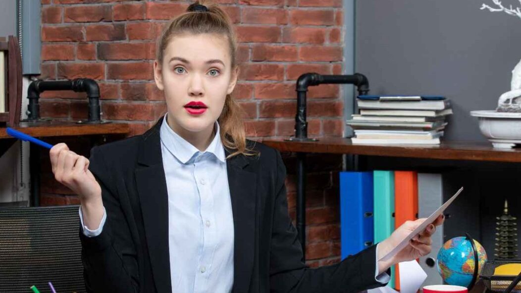 Confused professional woman sitting at a desk with documents, illustrating changes in USCIS rules for immigration fees.