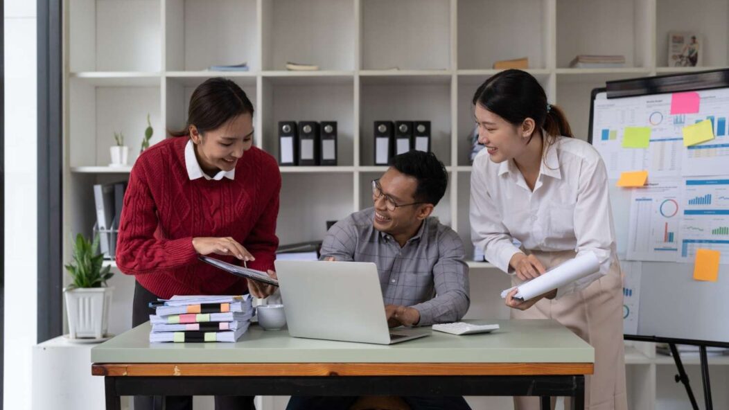 International students discussing self-employment opportunities on OPT with laptops and documents in a modern workspace.
