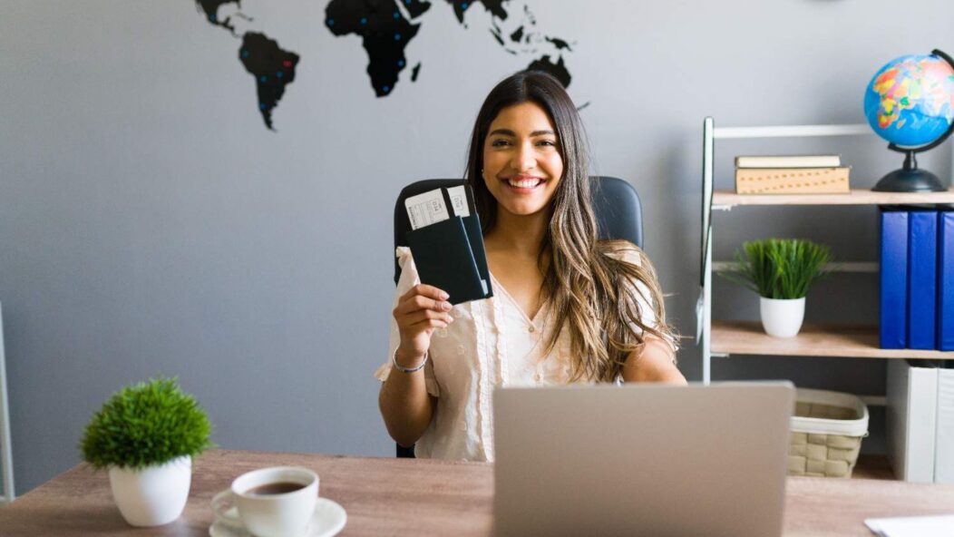 Smiling woman holding a passport with flight tickets at her desk, symbolizing new opportunities for H-1B visa holders starting businesses in the U.S.