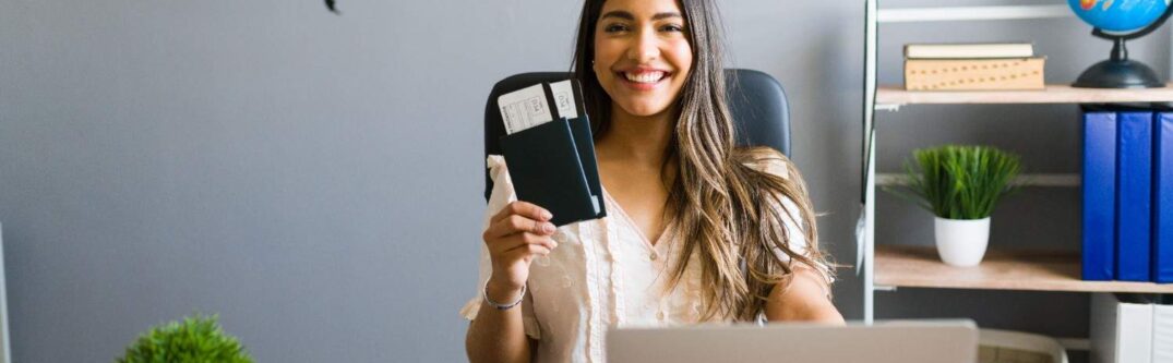 Smiling woman holding a passport with flight tickets at her desk, symbolizing new opportunities for H-1B visa holders starting businesses in the U.S.