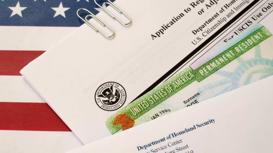Person reviewing a U.S. permanent resident card and application form on a desk.