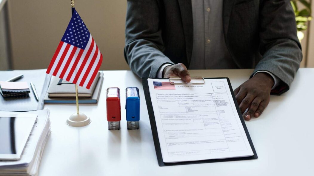 USCIS application forms with American flag and glasses on a wooden desk.