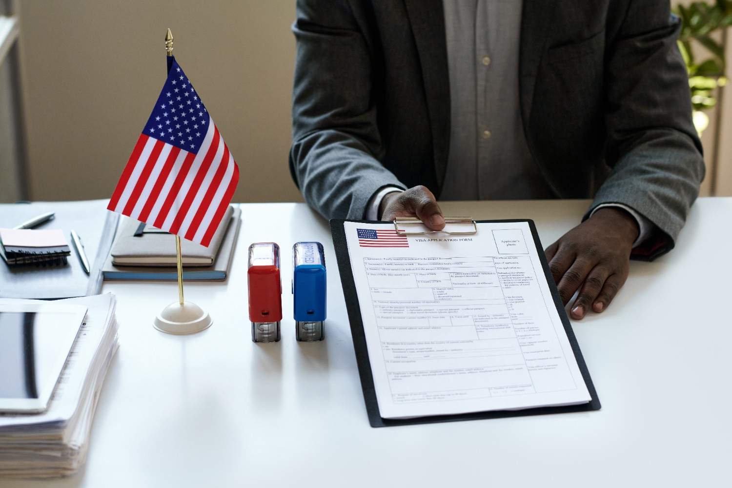 USCIS application forms with American flag and glasses on a wooden desk.