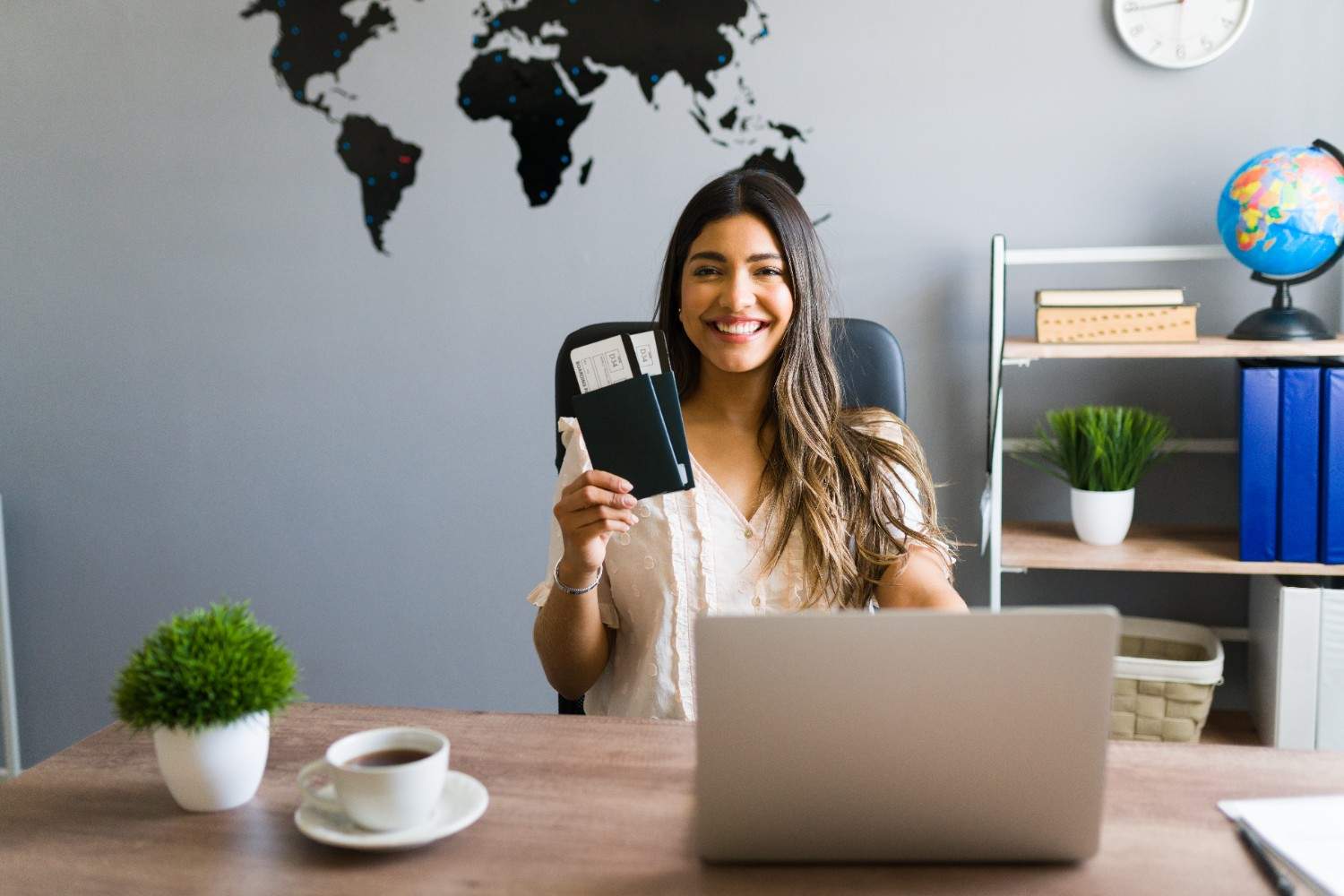 Smiling woman holding a passport with flight tickets at her desk, symbolizing new opportunities for H-1B visa holders starting businesses in the U.S.