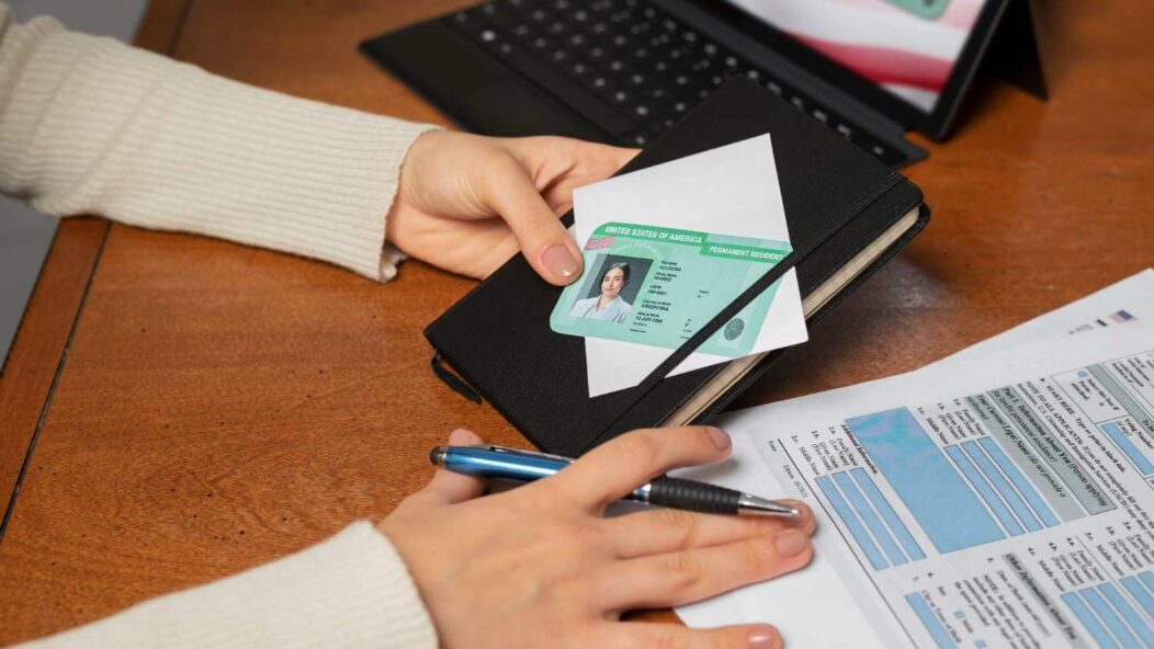 Person reviewing a U.S. permanent resident card and application form on a desk.