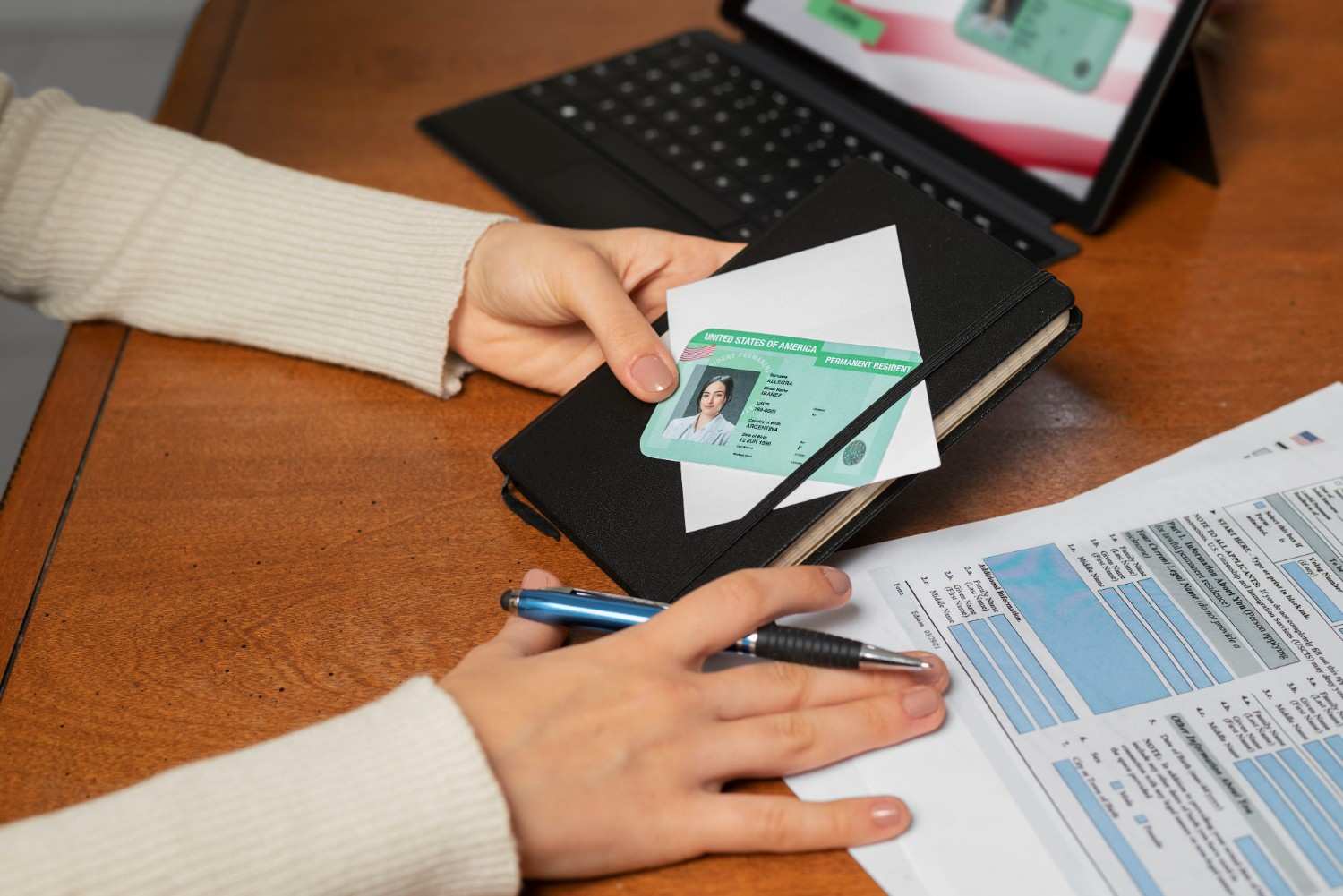 Person reviewing a U.S. permanent resident card and application form on a desk.