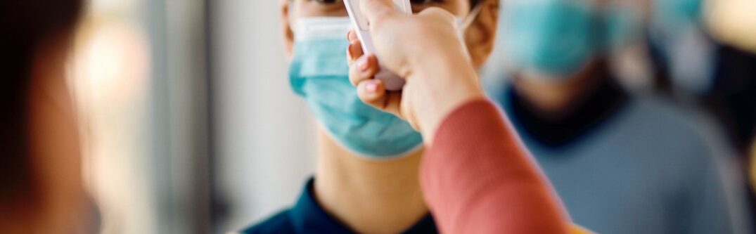 Person wearing a mask undergoing a temperature check during COVID-19 protocols