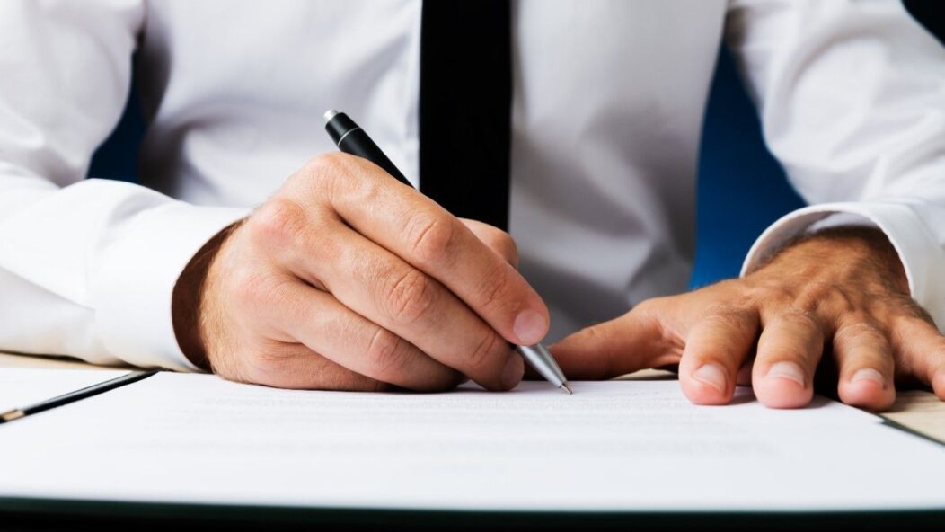 A professional in a suit signing official immigration documents, representing legal solutions for STEM OPT and H1B visa fraud implications.