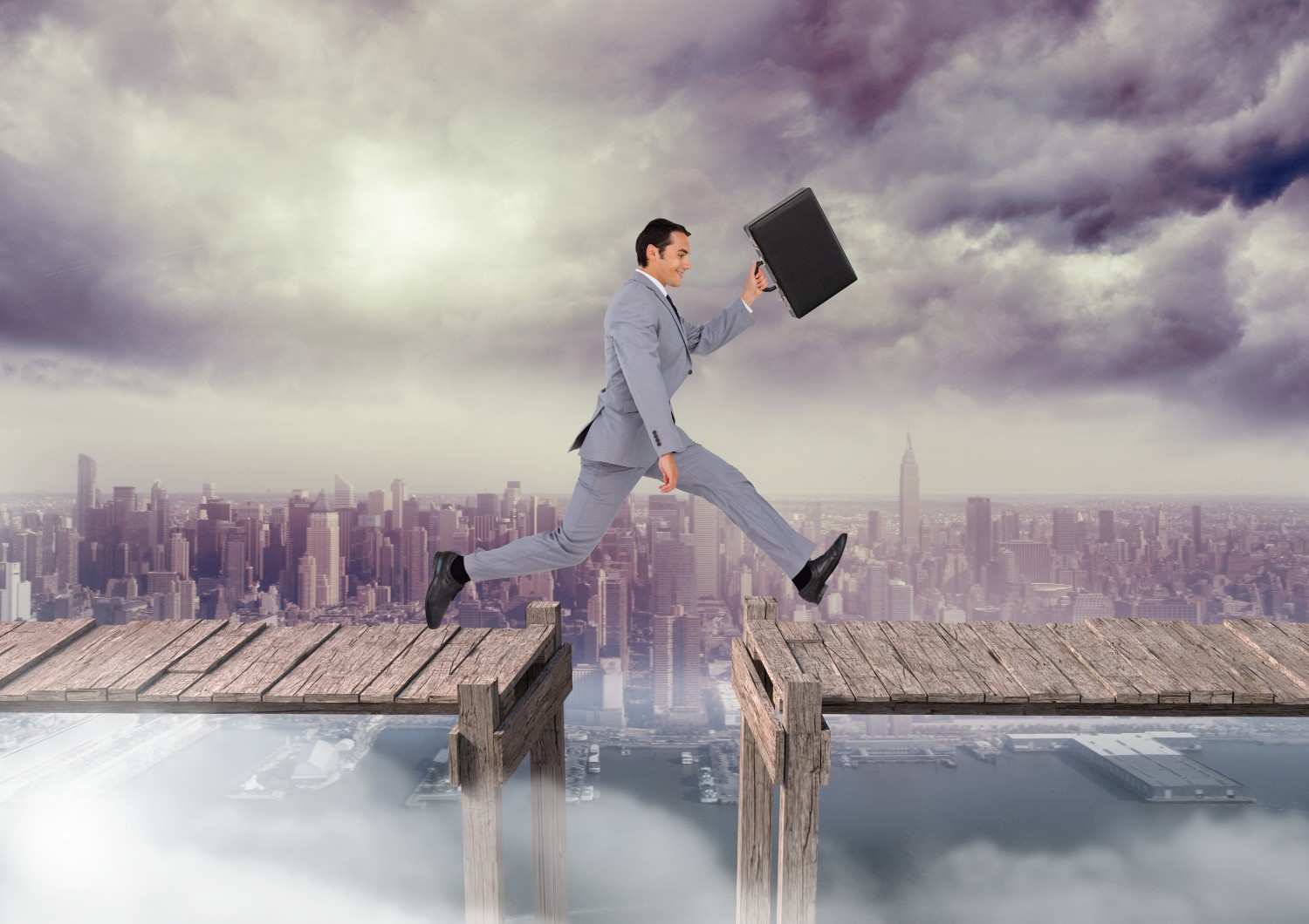 Businessman jumping across a broken bridge over a city skyline, symbolizing overcoming L-1A visa denial challenges and navigating the appeal process.