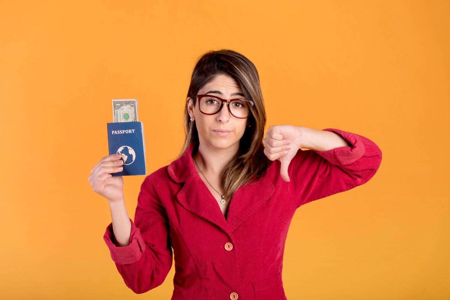 Visa denial fraud mark on immigration profile holding passport and money with thumbs down