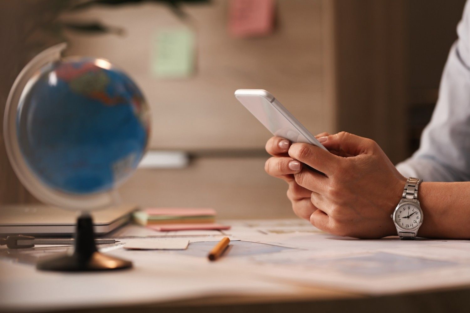 Person reviewing social media on smartphone, with a globe and documents in the background, symbolizing USCIS social media policy for immigration applications.