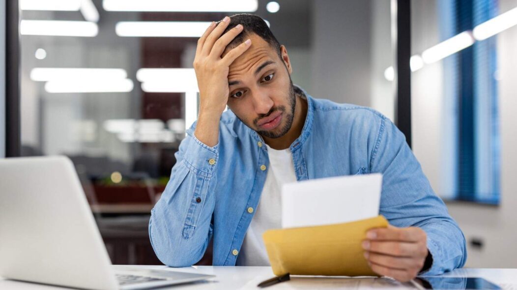 Frustrated man reading immigration rejection letter due to paperwork error, highlighting the risk of application mistakes.